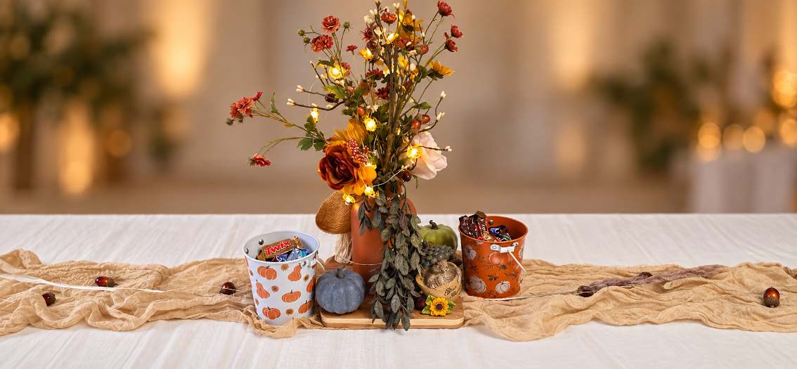 Autumn tablescape with lit branches, orange blooms and candy buckets.