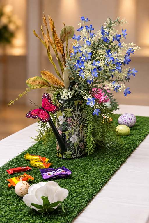 Watering can spilling spring flowers across a garden-themed table.