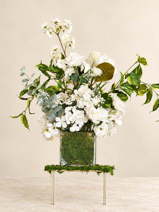 Loose garden-style centerpiece of white blooms and trailing greenery.